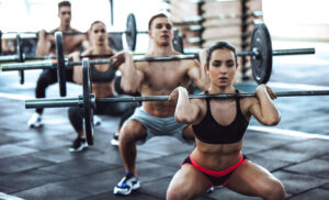 Group of sporty muscular people are working out in gym. Cross fit training. Handsome shirtless men and attractive women are doing exercises with barbells. Weightlifting.