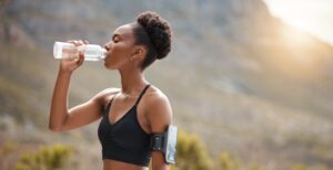 Health, fitness and black woman drinking water in nature for morning cardio, running or training at sunset. Exercise, wellness and African runner with sports, liquid or hydration for workout recovery