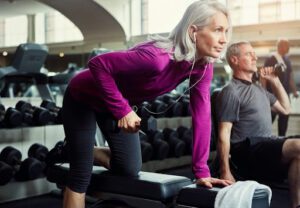 Older Woman exercising and lifting weights in gym.